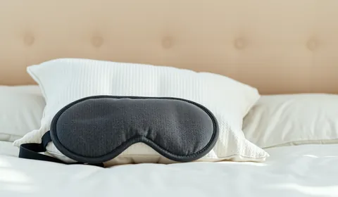 A white pillow with a grey sleep mask on a bed