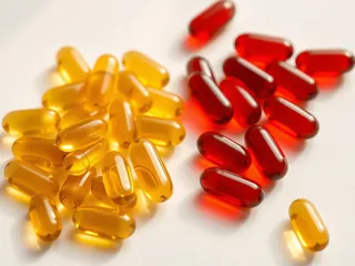 Golden fish oil softgels beside red krill oil softgels