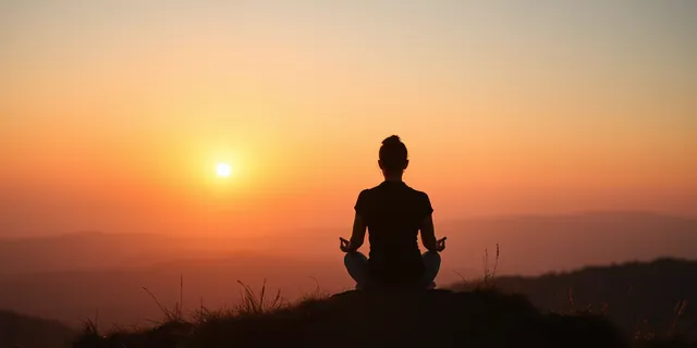 A person meditating on a mountain top at sunset
