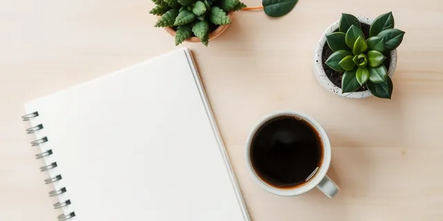 A coffee cup, an open notebook and a plant on a wooden desk