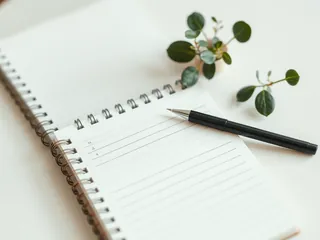 An open notebook with a pen beside a plant